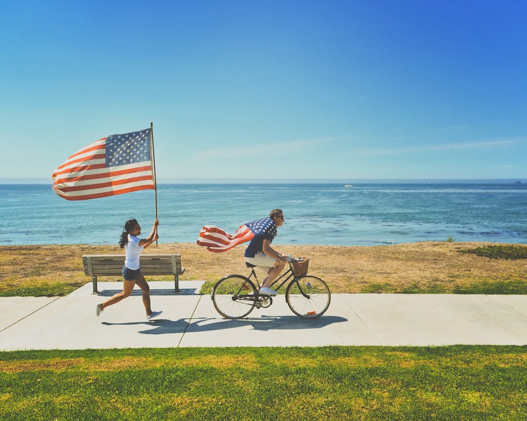 アメリカの国旗を掲げて自転車に乗る人々がビーチを行く